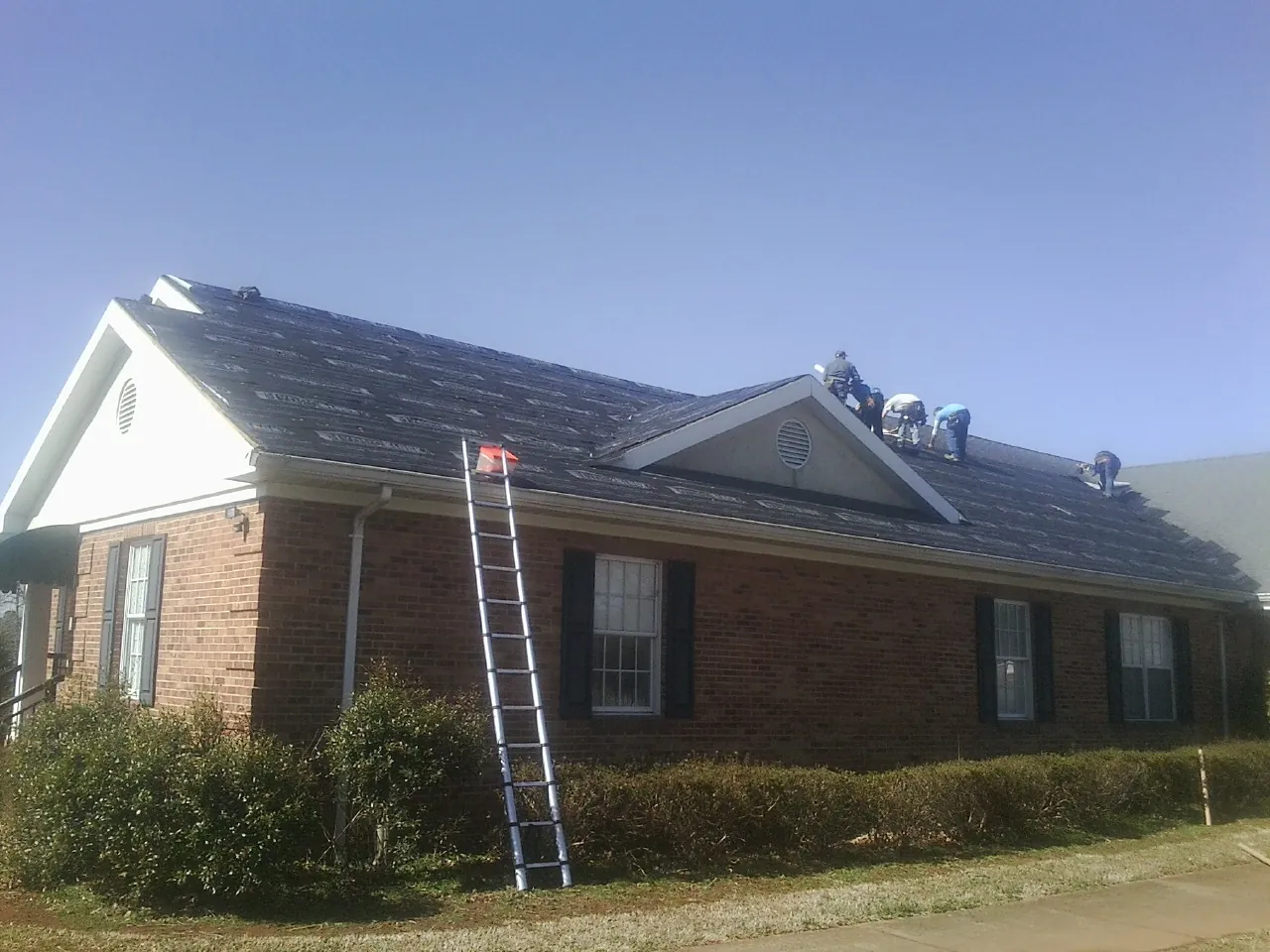 Crew tearing shingles off a brick ranch roof with a ladder set — Emergency Roof Repair work by our crew in Lawrenceville