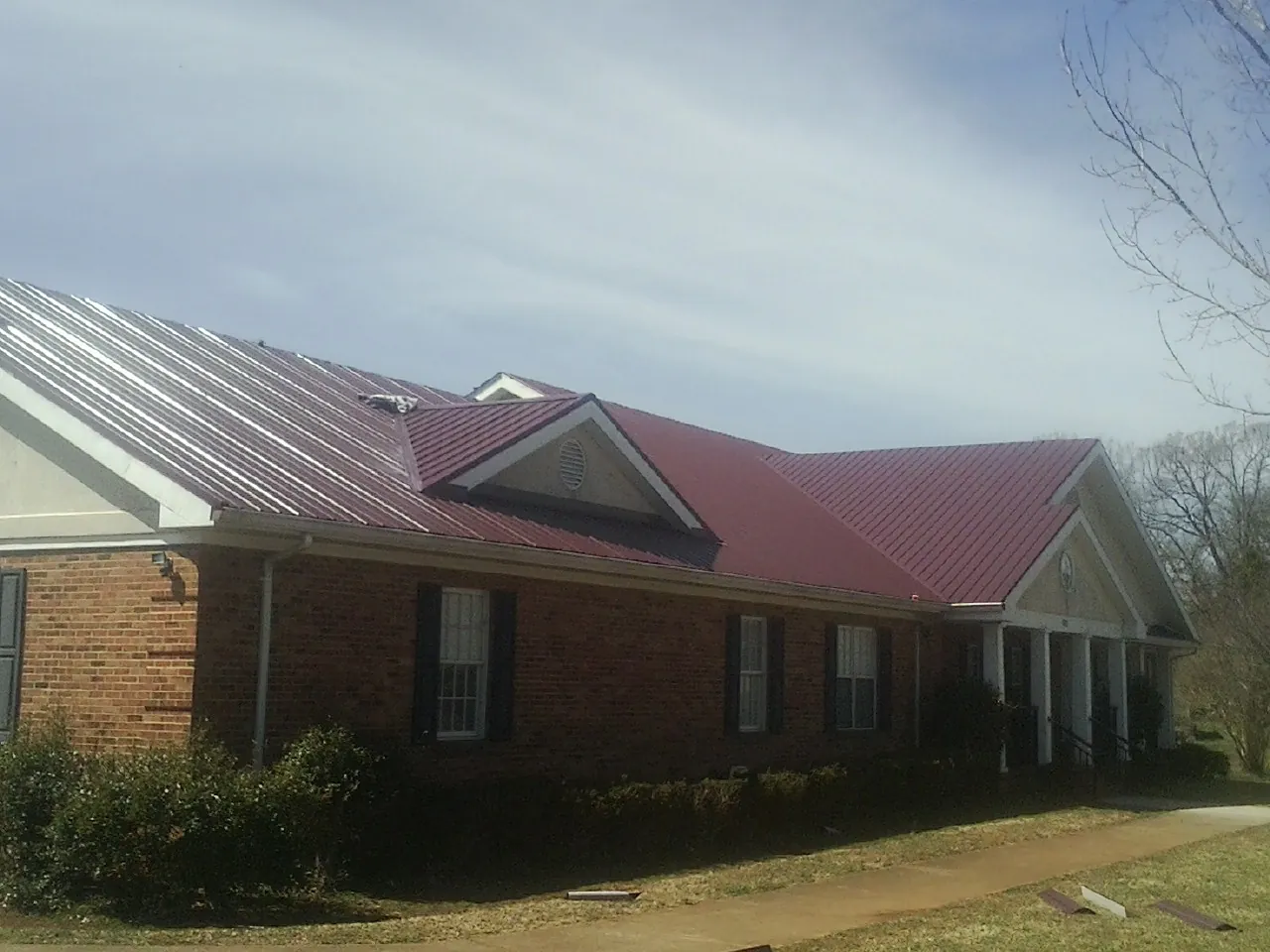 Red metal roof with gabled entries on a long brick building, from a Hail Damage Roof Repair job in Lawrenceville