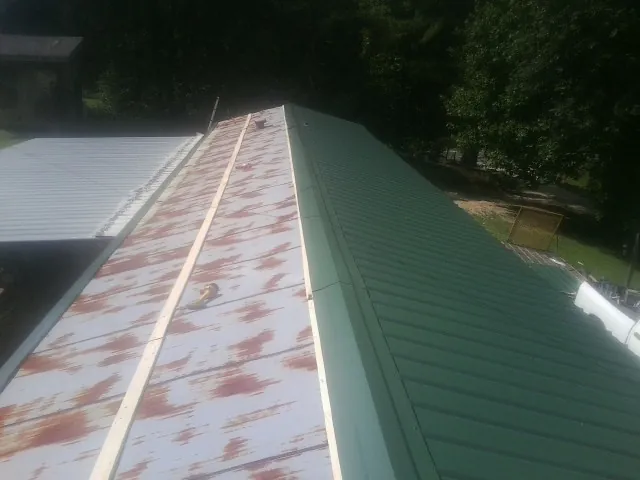Old rusted panels beside newly installed green metal roofing — Wind Damage Roof Repair by Roofing Brothers in Lawrenceville